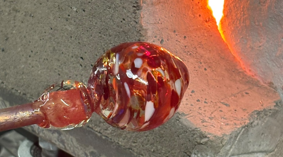 Molten glass on a blowpipe in front of a glowing furnace